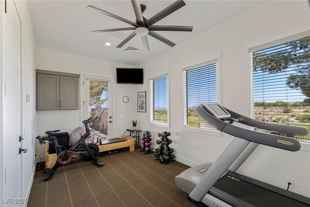 exercise area featuring dark carpet, ceiling fan, and a healthy amount of sunlight