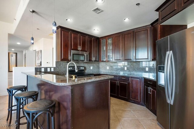 kitchen with appliances with stainless steel finishes, light stone counters, hanging light fixtures, a breakfast bar area, and light tile patterned flooring