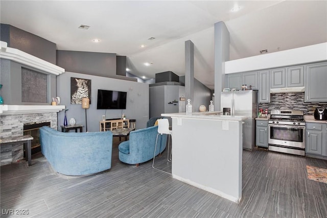 kitchen featuring gray cabinets, a kitchen island, a stone fireplace, decorative backsplash, and stainless steel appliances