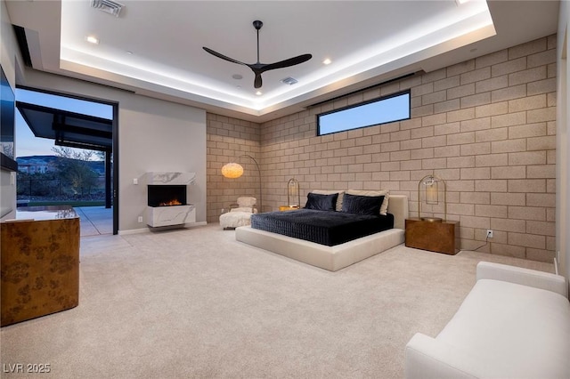 carpeted bedroom featuring a tray ceiling, ceiling fan, and a premium fireplace