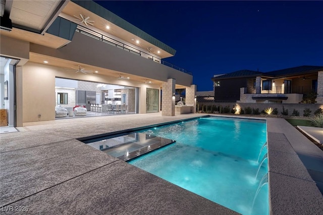 pool at night with a patio area, pool water feature, and ceiling fan