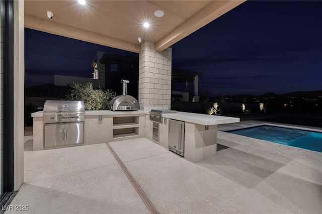 patio at twilight with an outdoor kitchen, area for grilling, and a fenced in pool