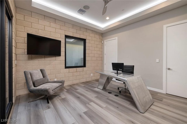 home office featuring light wood-type flooring and a raised ceiling