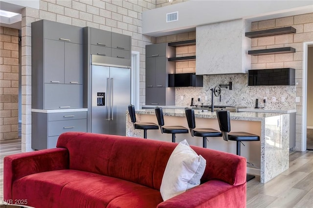 kitchen with a breakfast bar, gray cabinets, built in refrigerator, and light hardwood / wood-style floors