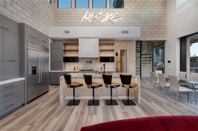 kitchen featuring gray cabinetry, a breakfast bar, a high ceiling, and built in refrigerator