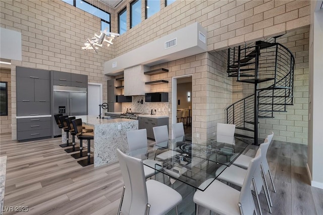 dining space with sink, light hardwood / wood-style floors, a high ceiling, and a notable chandelier