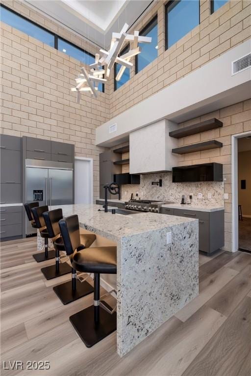 kitchen with decorative backsplash, light stone counters, stainless steel built in fridge, a high ceiling, and light hardwood / wood-style floors