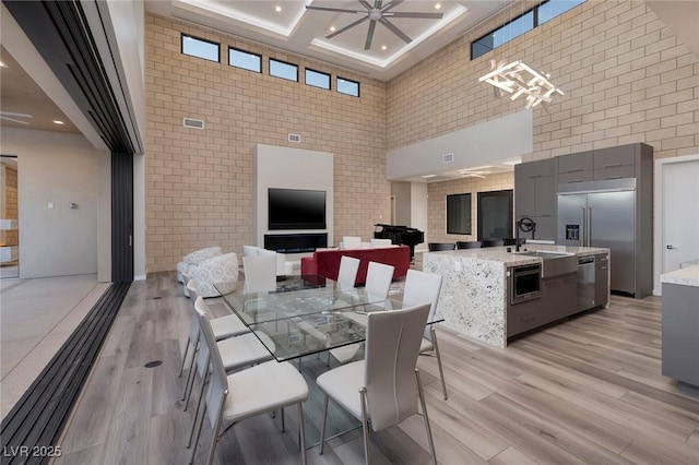 dining room featuring a wealth of natural light, ceiling fan, coffered ceiling, a towering ceiling, and light wood-type flooring