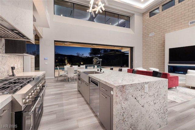 kitchen featuring decorative backsplash, a towering ceiling, stainless steel appliances, sink, and a center island with sink