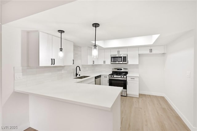 kitchen with kitchen peninsula, stainless steel appliances, sink, white cabinetry, and hanging light fixtures