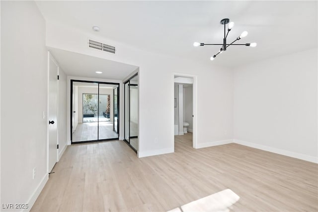 spare room featuring light wood-type flooring and a notable chandelier