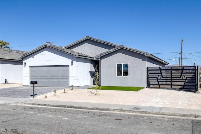 ranch-style house with a garage, a tile roof, decorative driveway, a gate, and stucco siding