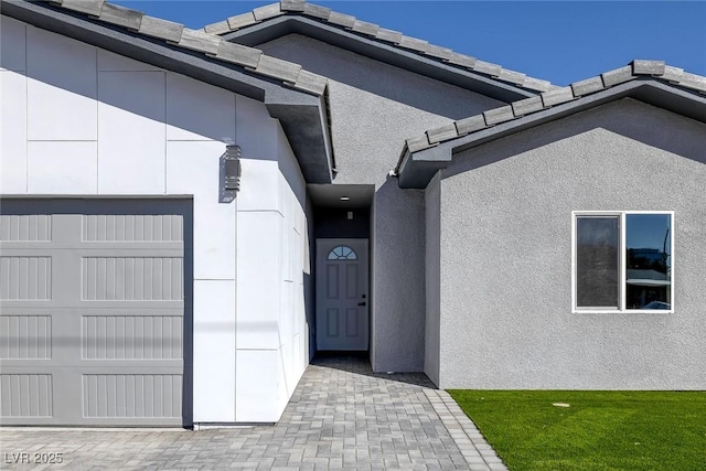 view of exterior entry with an attached garage and stucco siding