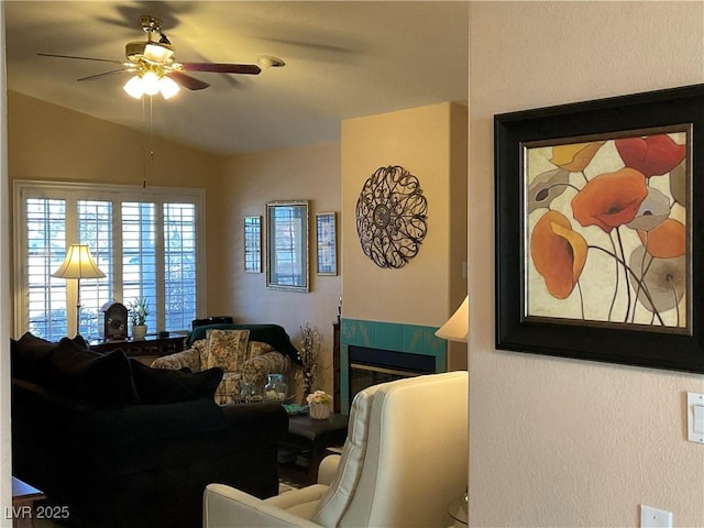 living room featuring vaulted ceiling, ceiling fan, and a tiled fireplace