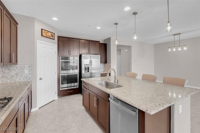 kitchen featuring an island with sink, appliances with stainless steel finishes, a sink, and hanging light fixtures