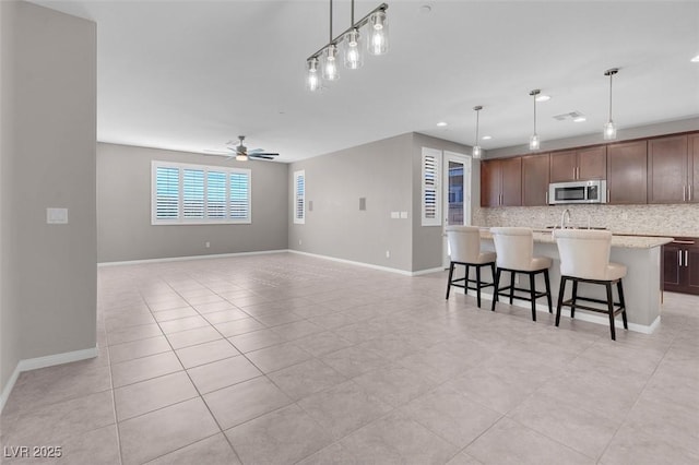 kitchen with stainless steel microwave, backsplash, open floor plan, an island with sink, and a kitchen bar