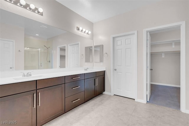 bathroom with a sink, baseboards, double vanity, a stall shower, and a walk in closet