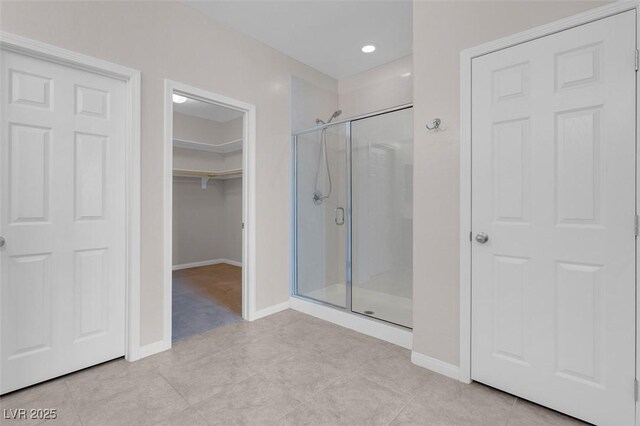 bathroom featuring tile patterned flooring, a shower stall, baseboards, and a spacious closet