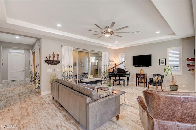 living room with a tray ceiling, ceiling fan, and light hardwood / wood-style floors