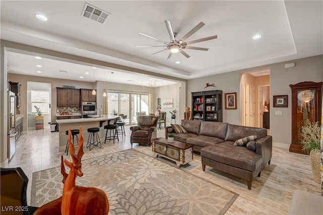 living room with a tray ceiling, ceiling fan, and light hardwood / wood-style flooring