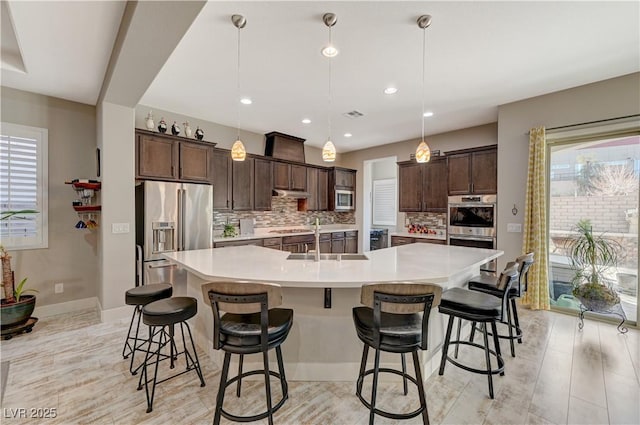 kitchen with decorative backsplash, stainless steel appliances, sink, pendant lighting, and a large island with sink