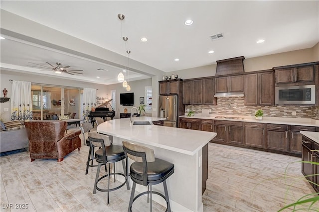 kitchen with a large island, ceiling fan, hanging light fixtures, backsplash, and appliances with stainless steel finishes