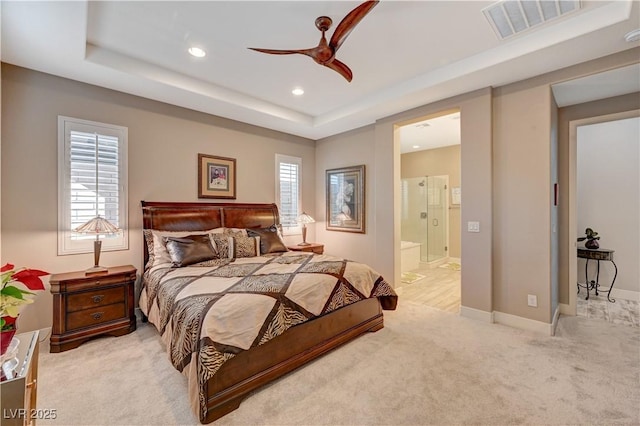 carpeted bedroom with a tray ceiling, connected bathroom, and ceiling fan