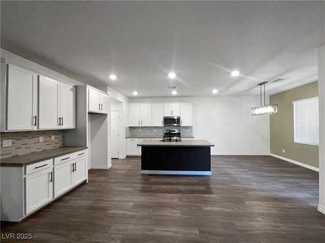 kitchen featuring appliances with stainless steel finishes, a kitchen island, dark wood-type flooring, decorative light fixtures, and white cabinetry