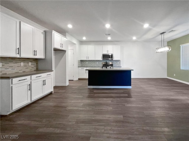 kitchen with dark wood-type flooring, a center island with sink, white cabinets, and pendant lighting