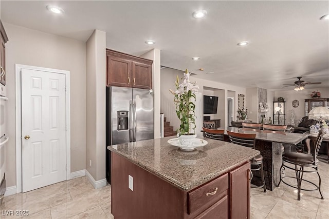 kitchen featuring stainless steel refrigerator with ice dispenser, ceiling fan, dark stone counters, and a center island