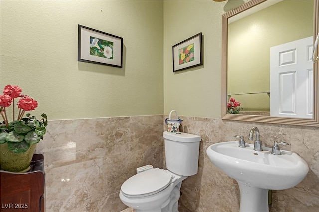 bathroom with toilet, tile walls, and sink