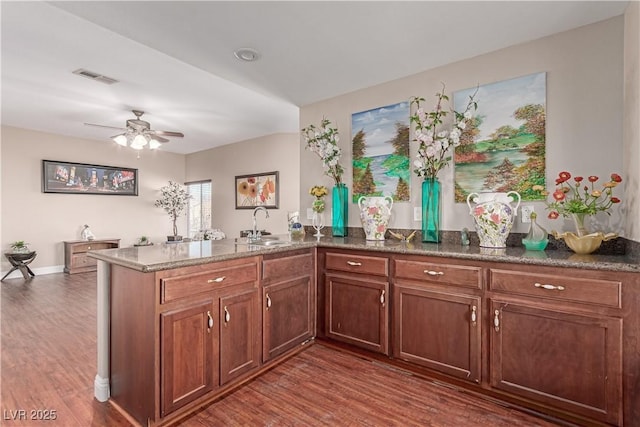 kitchen with ceiling fan, dark hardwood / wood-style floors, kitchen peninsula, sink, and dark stone counters