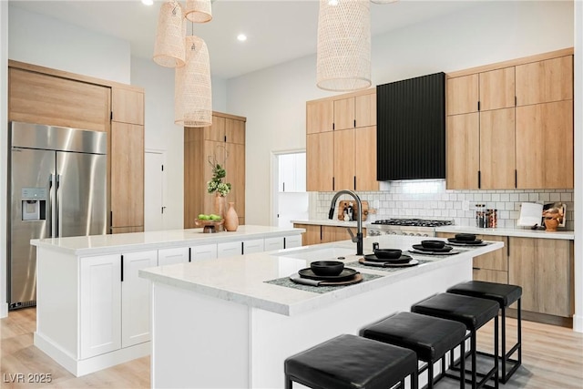 kitchen with decorative backsplash, appliances with stainless steel finishes, exhaust hood, sink, and a center island with sink