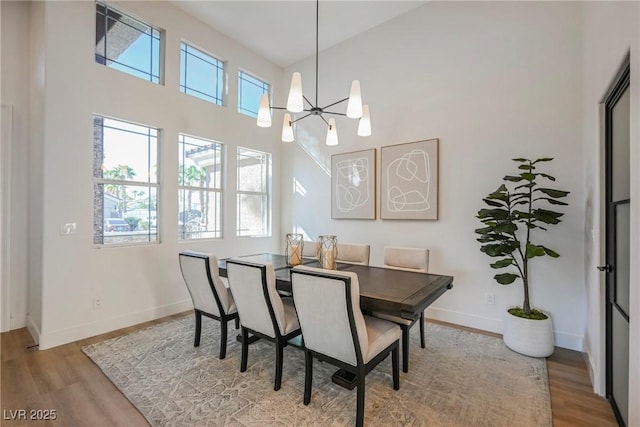 dining area featuring a healthy amount of sunlight, light wood-type flooring, a high ceiling, and an inviting chandelier