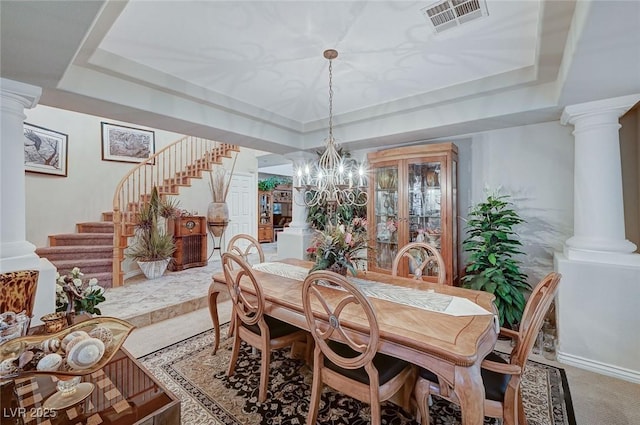 carpeted dining area featuring a notable chandelier, a raised ceiling, and ornate columns