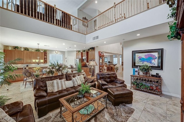 living room with a towering ceiling, ornate columns, a wealth of natural light, and a notable chandelier