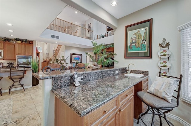 kitchen featuring a kitchen bar, dark stone counters, stainless steel oven, sink, and a center island