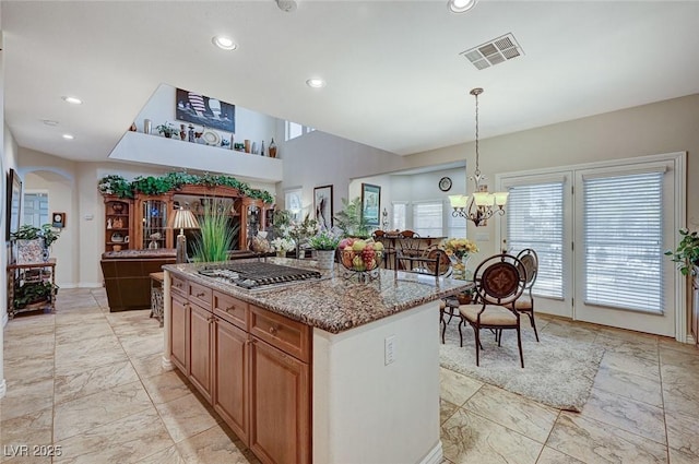 kitchen featuring an inviting chandelier, light stone countertops, decorative light fixtures, a kitchen island, and stainless steel gas cooktop