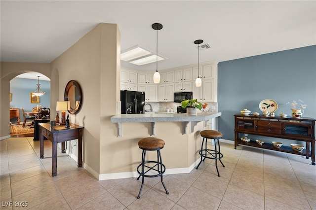 kitchen with a kitchen breakfast bar, decorative backsplash, light tile patterned flooring, and black appliances