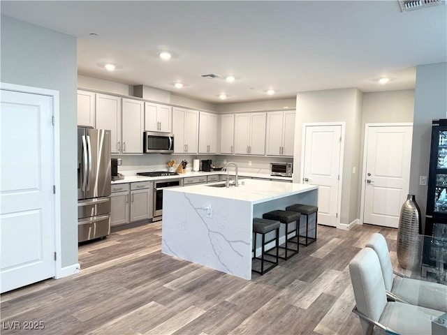 kitchen featuring a center island with sink, sink, a kitchen bar, wood-type flooring, and stainless steel appliances