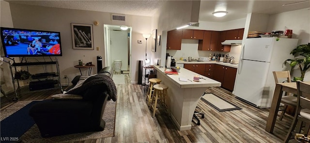 kitchen featuring sink, white refrigerator, a textured ceiling, a breakfast bar area, and light wood-type flooring