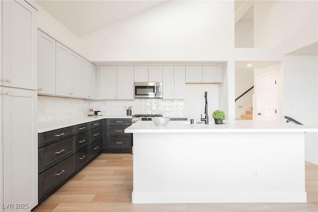 kitchen with light wood-type flooring, appliances with stainless steel finishes, a kitchen island, white cabinets, and backsplash