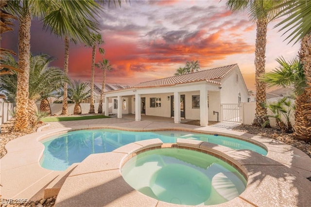 pool at dusk with a patio area and an in ground hot tub