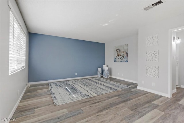 spare room featuring wood finished floors, visible vents, and baseboards