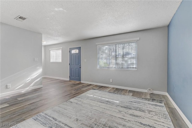 unfurnished room featuring baseboards, wood finished floors, visible vents, and a textured ceiling