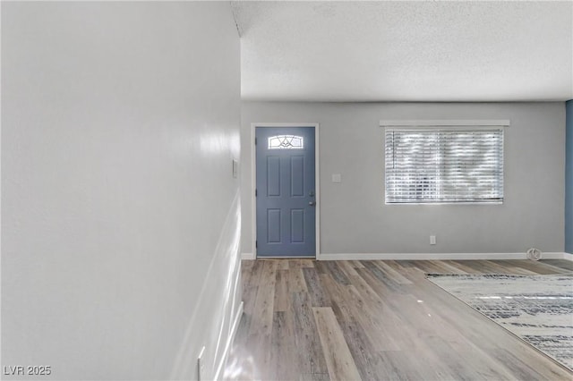 foyer entrance featuring baseboards, a textured ceiling, and wood finished floors