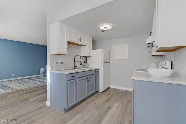 kitchen with extractor fan, light wood-type flooring, light countertops, freestanding refrigerator, and a sink