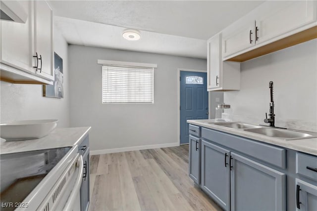 kitchen featuring baseboards, light wood finished floors, electric range, a sink, and light countertops