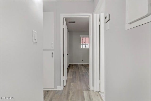 hall featuring visible vents, light wood-style flooring, and baseboards