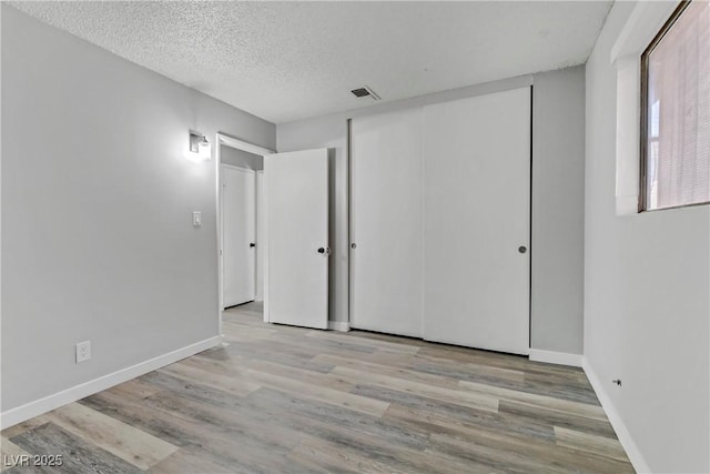 unfurnished bedroom with visible vents, a textured ceiling, baseboards, and wood finished floors